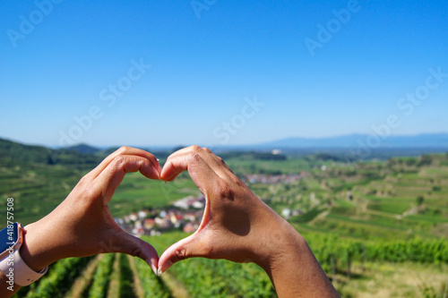 Close-up of a woman's hands forming a heart around a beautiful village surrounded by vineyards at Kaiserstuhl, Germany. photo