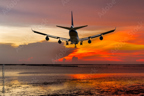 rear view commercial passenger aircraft or cargo transportation airplane fly over coast of sea after takeoff from airport in evening with red sky