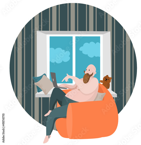 A large fat man with a beard and mustache works in a laptop while sitting in a chair by the window.