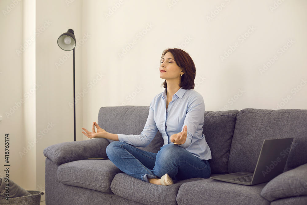 Caucasian middle age self-employed woman entrepreneur meditating on home sofa Caucasian middle age self-employed woman entrepreneur meditating on home sofa