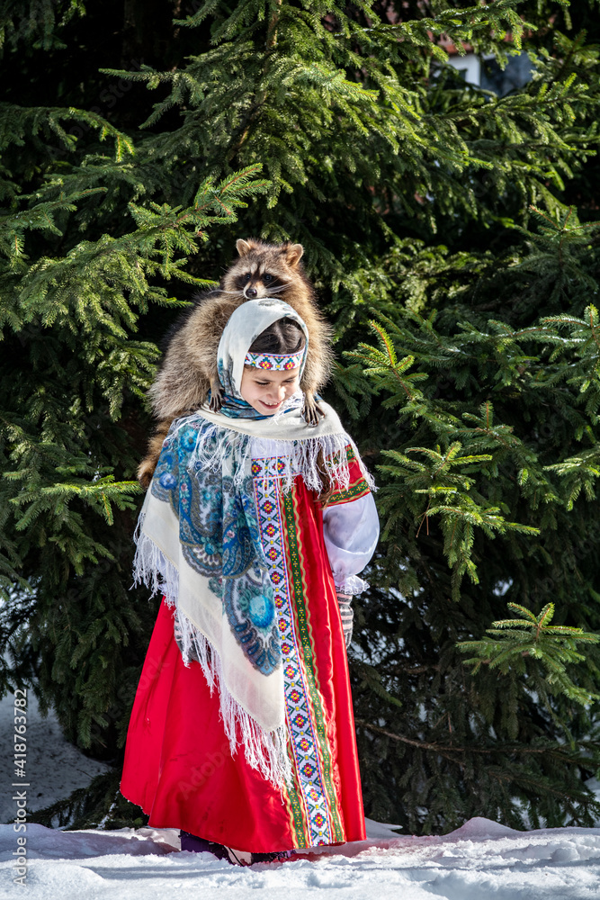 beautiful girl in a red sundress plays with a gray raccoon in a winter park