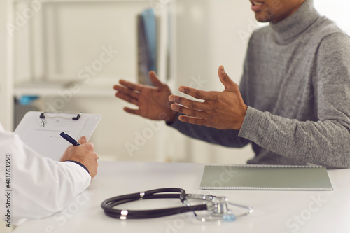 Black man patient sitting and explaining health complaints to man doctor during consultation in medical clinic office, cropped composition. Medicare, healthcare, communication with doctor