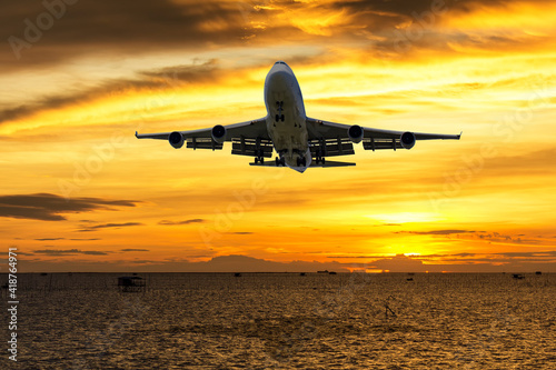 front image commercial passenger aircraft or cargo transportation airplane fly over coast of sea and spread the wheel prepare landing to airport in evening with sun and golden sunset seascape view
