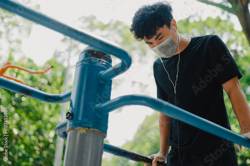 Social distancing. Young asian man in protective masks working out in park outdoors. Doing push-up and pull-up exercises. Sport in quarantine. Covid-19. Protection.