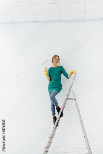 A young girl on the stairs paints a white wall with a roller. Repair of the interior.