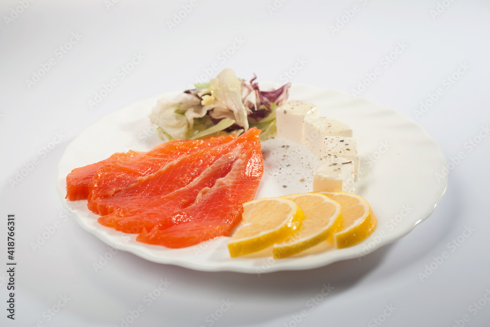 slices of salted salmon with cream cheese lemon and greens in a white plate on a white background