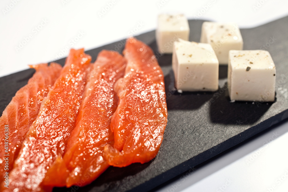 slices of salmon cubes of cream cheese on a black slate board on a white background