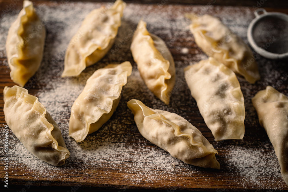 Fototapeta premium Asian raw dumplings on on wooden cutting board. Traditional chinese dim sum dumplings.