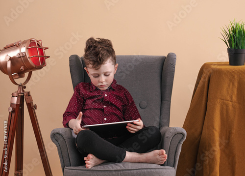 Concepto de infancia y personas - hermoso niño con tableta sentada en el sofá  photo