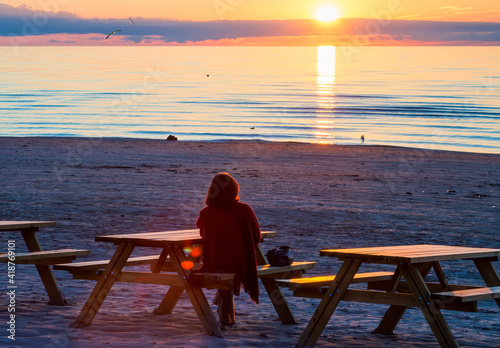 Silhouette of a woman sitting on sandy beach at sunset, Baltic Sea, Europe