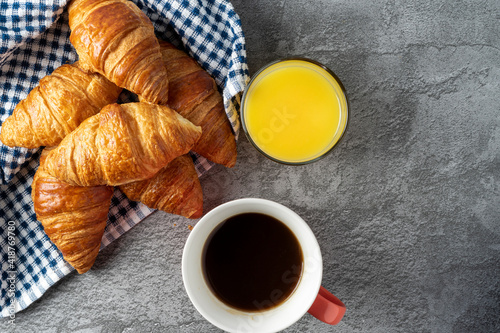 Top view of several small croissants on a blue checkered cloth next to a cup of coffee and orange juice. Copy space