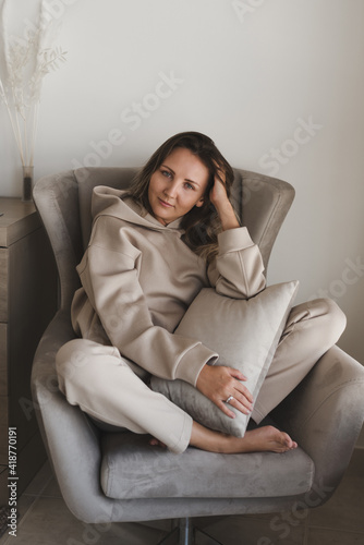Woman dressed in comfy loungewear of grey color sitting in a cozy and comfortable armchair. Casual outfit. Home clothing. Female's portrait photo
