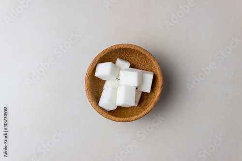 Sugar cubes in a wooden plates in center of the kitchen table. Top view