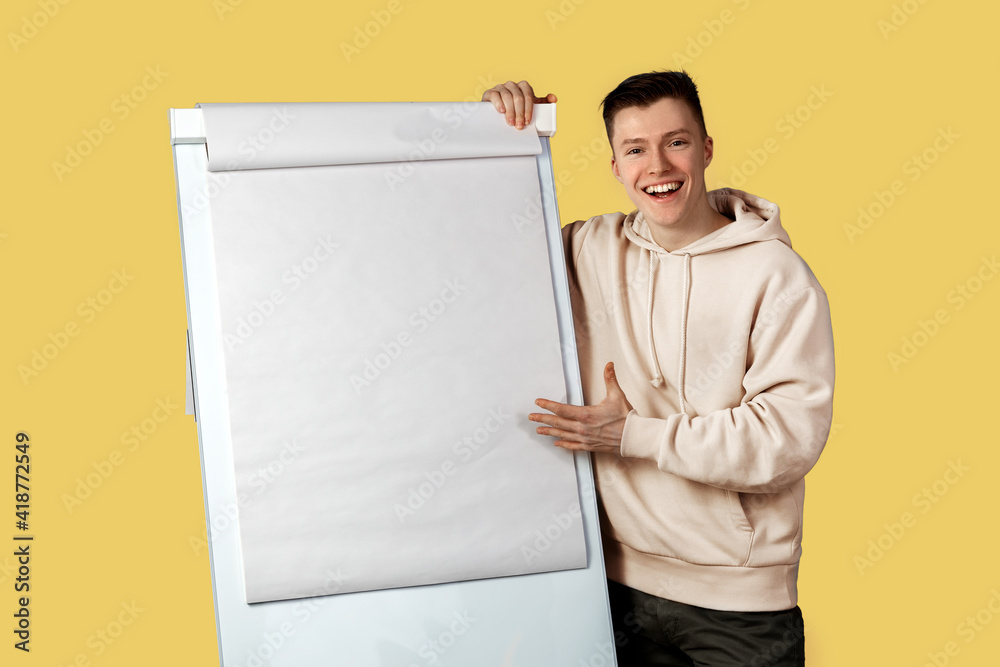A young businessman With a smile on his face stands near the whiteboard and makes a presentation. Yellow background. High quality photo A young businessman With a smile on his face stands near the whiteboard and makes a presentation. Yellow background. High quality photo