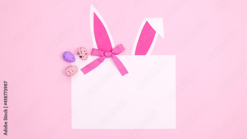 Creative Easter paper card note appear with bunny ears, bow and eggs on pastel pink background. Stop motion flat lay Creative Easter paper card note appear with bunny ears, bow and eggs on pastel pink background. Stop motion flat lay