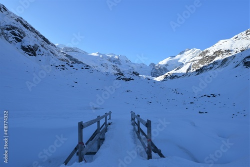 Panorama of the Bernina group with Piz Bernina and Morteratsch glacier and snow-covered wooden bridge with a bright blue sky and sunshine 