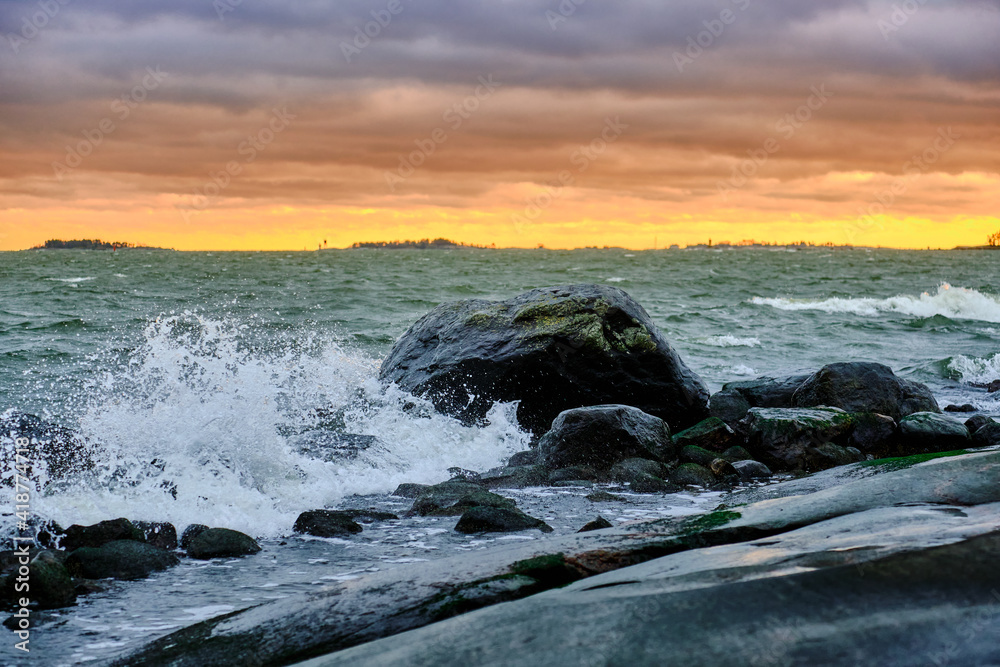 Sea waves rolling on stones, cloudy sunset sky on the background. The Nordic nature. Baltic sea.