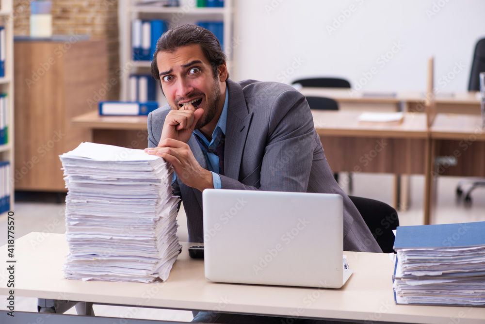 Young male employee unhappy with excessive work in the office Young male employee unhappy with excessive work in the office