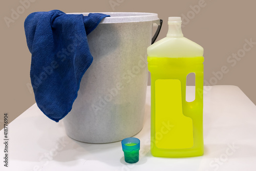 a bucket with a rag and an open bottle of detergent on a white table