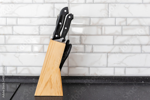 set of kitchen knives in a wooden stand on a white tile background