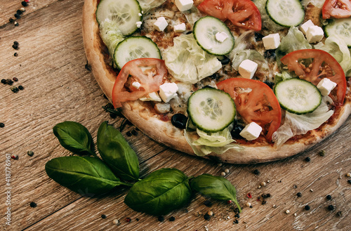 Vegetable pizza with mozzarella, fresh tomatoes and cucumber. Green basil leaves