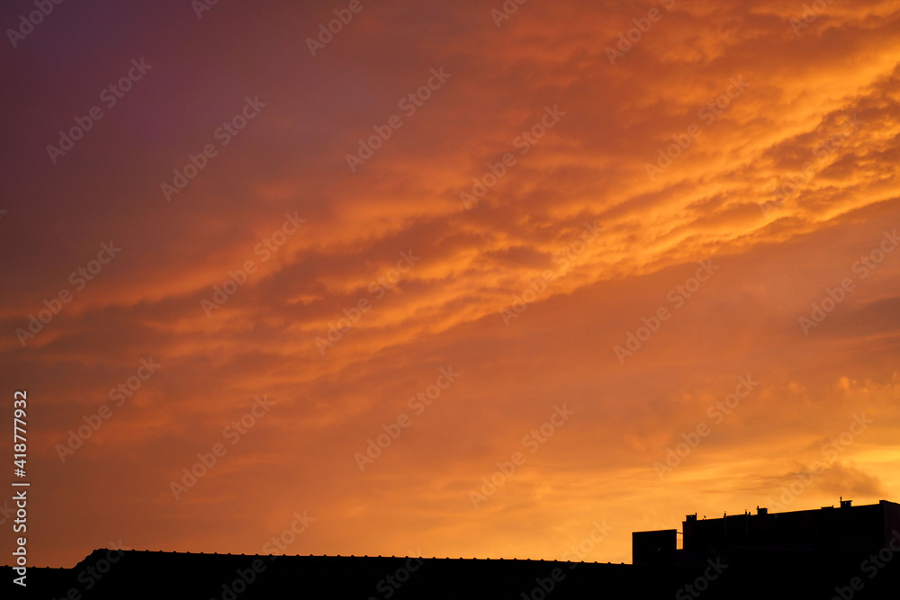 orange sky with clouds in the evening against the backdrop of rooftops . view from the window orange sky with clouds in the evening against the backdrop of rooftops . view from the window