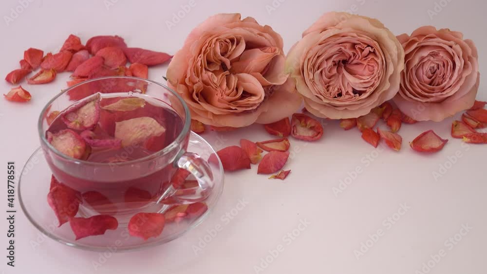 Rose petals float in a cup of tea against the background of roses and petals lying on the table Rose petals float in a cup of tea against the background of roses and petals lying on the table