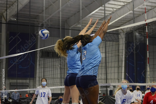 Female volleyball players double block during an indoor match
