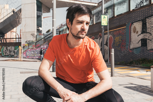 Young man wearing sportswear squatting resting outdoors