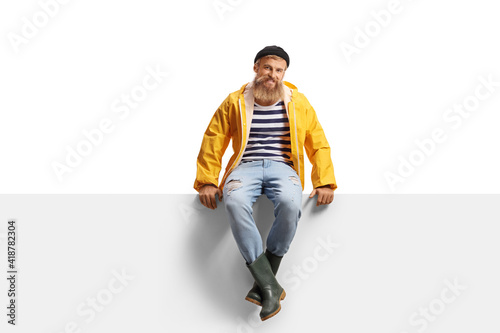 Bearded guy fisherman with a yellow rain coat sitting on a panel photo