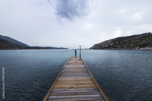 A girl stands on the pier and looks at the sea