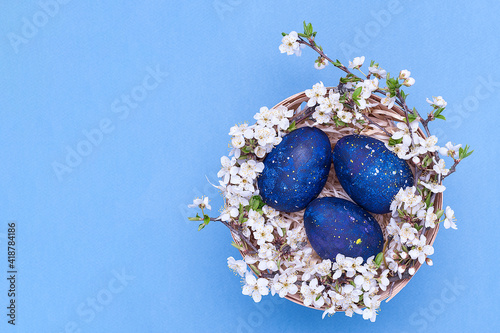 Obraz na płótnie Blue easter eggs in a basket with flowers on a blue background. Horizontal photograph. Top view w salonie