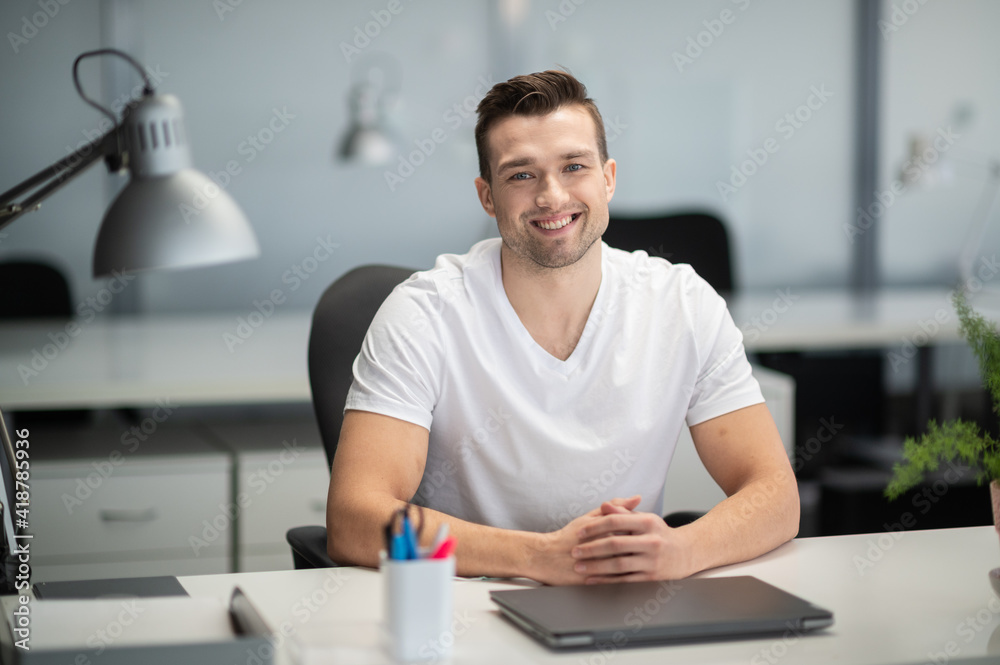 A young manager sits at a desk in the office and smiles for a photo. A young manager sits at a desk in the office and smiles for a photo.