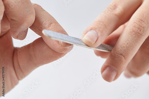 A woman does a manicure at home and uses a nail file to remove old gel polish from her nails. Close-up of a hand using a nail buffer when performing a manicure  polishing nails at home.
