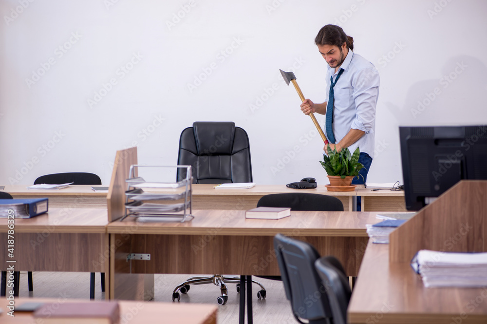 Young male furious employee holding hatchet in the office Young male furious employee holding hatchet in the office