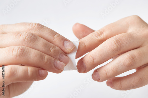 The girl cleans the nail plate with a manicure napkin during nail treatment. The girl makes a manicure at home. Nail treatment on an isolated background. Close-up.