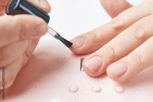 The girl applies a primer before coating the gel polish on her nails. The girl makes a manicure at home. Manicure with gel polish on an isolated background. Close-up.