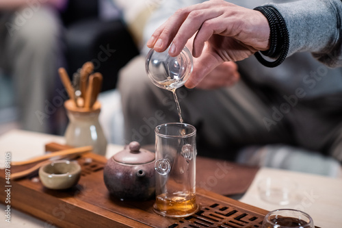 Close-up of a traditional oriental tea ritual. A man pours black ripe tea from a flask into a tasting cup. Blurry background