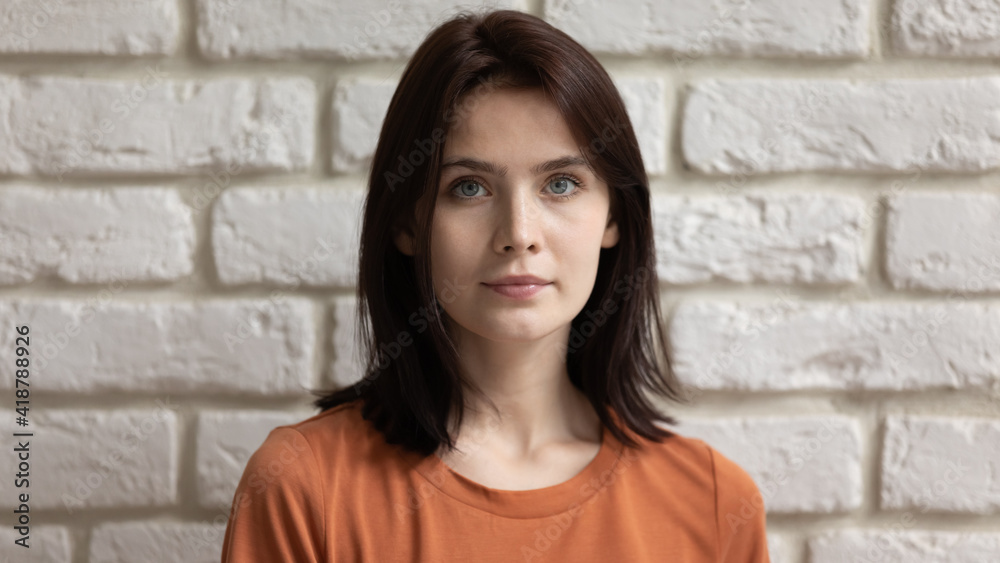 Beauty wearing casual. Profile picture of calm pretty millennial lady against white stone wall. Headshot portrait of young teenage female with dark straight hair beautiful face with healthy clear skin