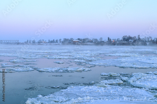 White snow-covered ice floes float along the wide river Neman. Ice drift in the fog at dawn. Winter in Europe