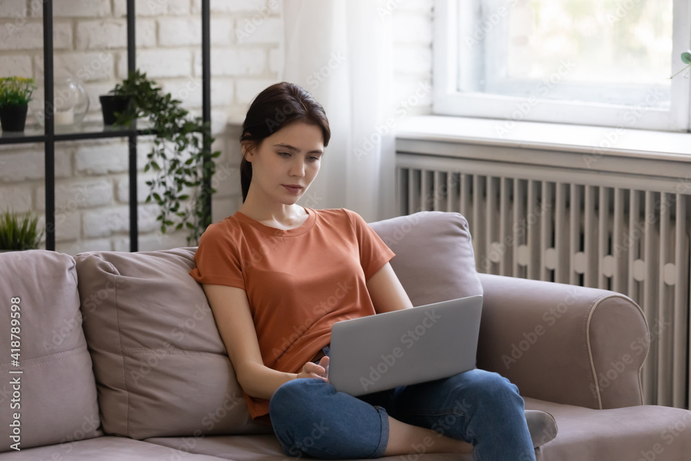 Engaged in online activity. Focused young female working from home sit on comfy sofa type message on laptop write email. Busy millennial woman freelancer study electronic documents confer in web app Engaged in online activity. Focused young female working from home sit on comfy sofa type message on laptop write email. Busy millennial woman freelancer study electronic documents confer in web app