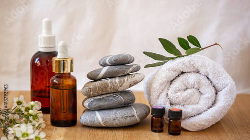 Dark glass vessel , essential oil cosmetic for skin care, massage and spa at home. Stack of stones, towel white flowers on a wooden table. 
