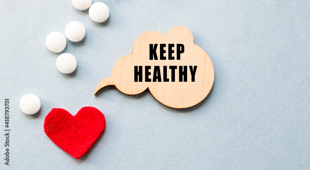 The inscription KEEP HEALTHY on a wooden template, against the background of scattered pills and a red heart. Medical concept. The inscription KEEP HEALTHY on a wooden template, against the background of scattered pills and a red heart. Medical concept.