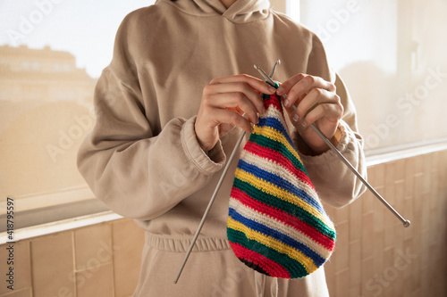 Young female knitting colourful hat with needles, wearing tracksuit, sustainable cloths, homemade and Eco friendly fabric photo