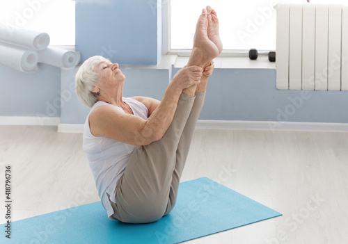 an old, elderly woman of 85 years old does a v-up exercise, a yoga exercise.Health, activity of the elderly concept