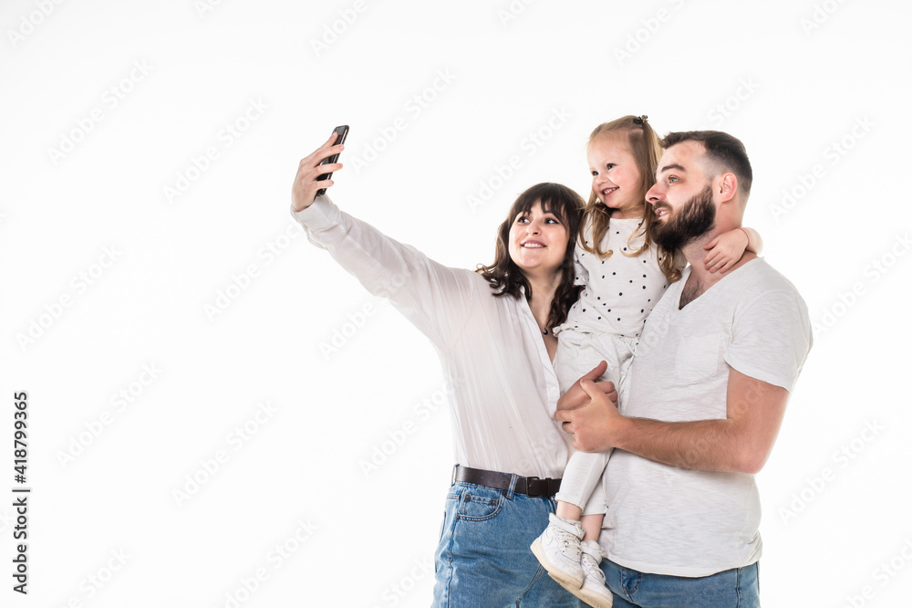 Full length portrait of a young family with a child standing together and taking a selfie isolated over white background