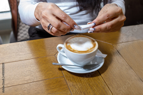 A customer in a cafe pours sugar into a cup of coffee.