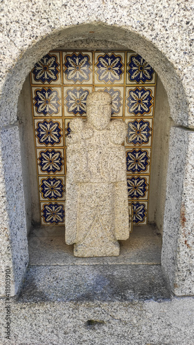 An old medieval sculpture with the figure of a saint in a large mansion estate near Esposende, Portugal. Rusty iron wheel of old mill water. Religious Figure.