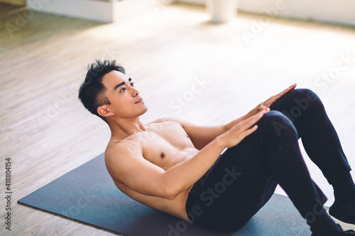 Muscular Asian young man doing exercises on floor at home