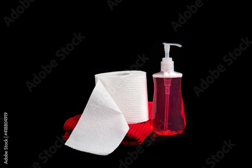 a roll of toilet paper and a bottle of red liquid hand soap and a red towel isolated on black 